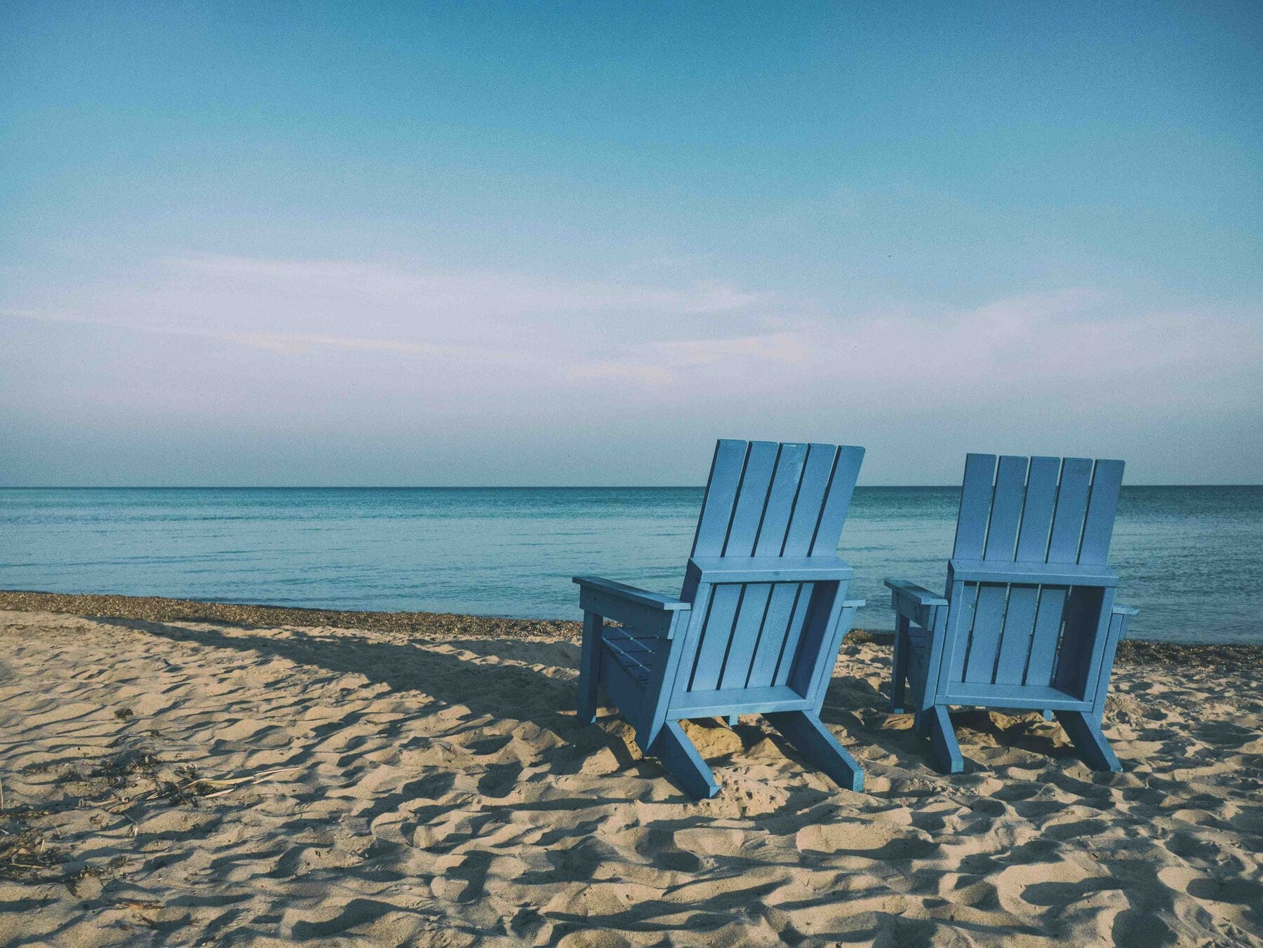 2 deckchairs on a beach facing out to sea to represent retirement